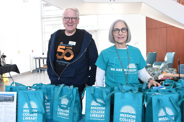 Two Mission employees handing out library bags